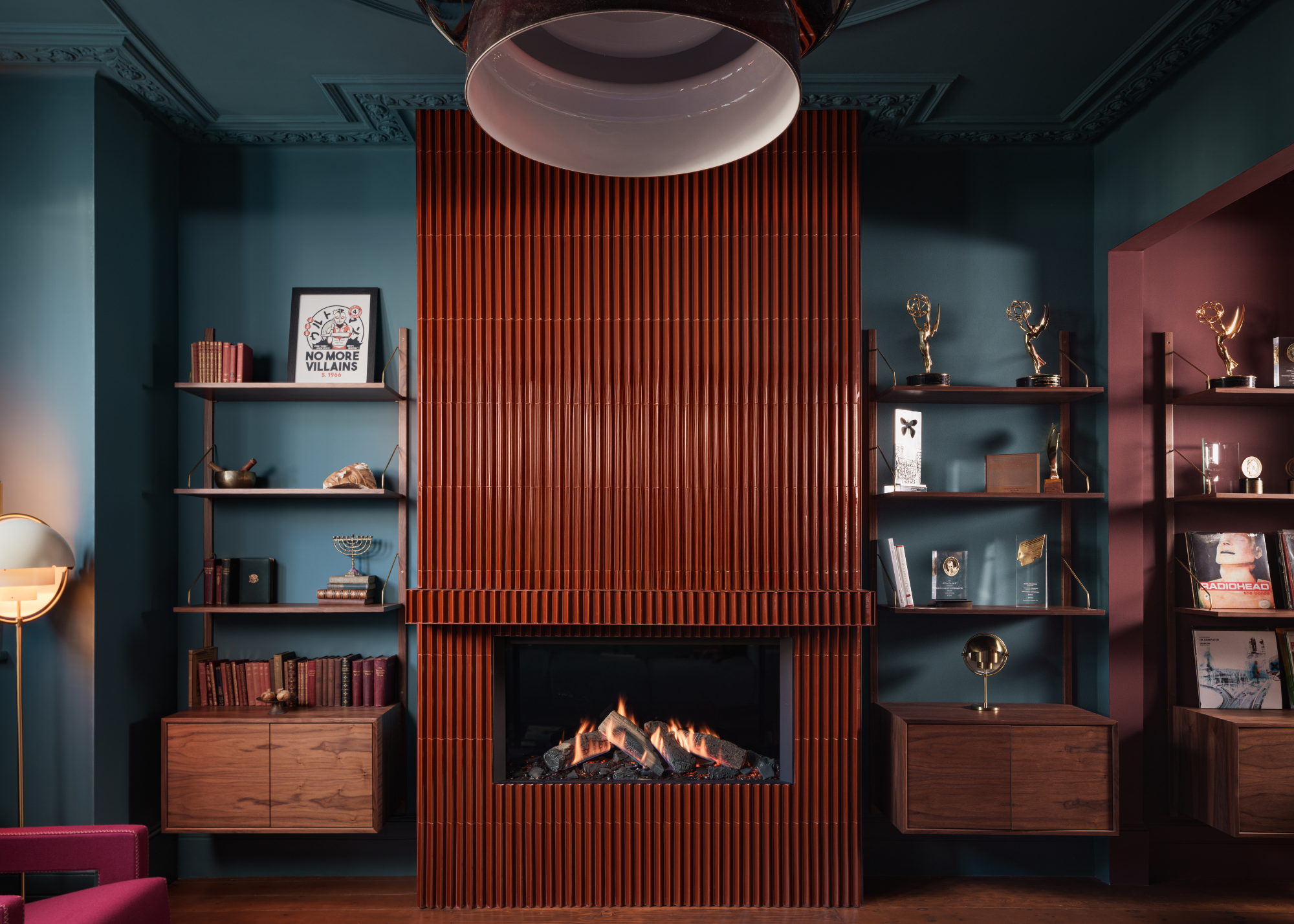 A rust brown-red tiled fireplace in a modern living room with tiles going right up to the ceiling with open shelving either side and teal-painted walls