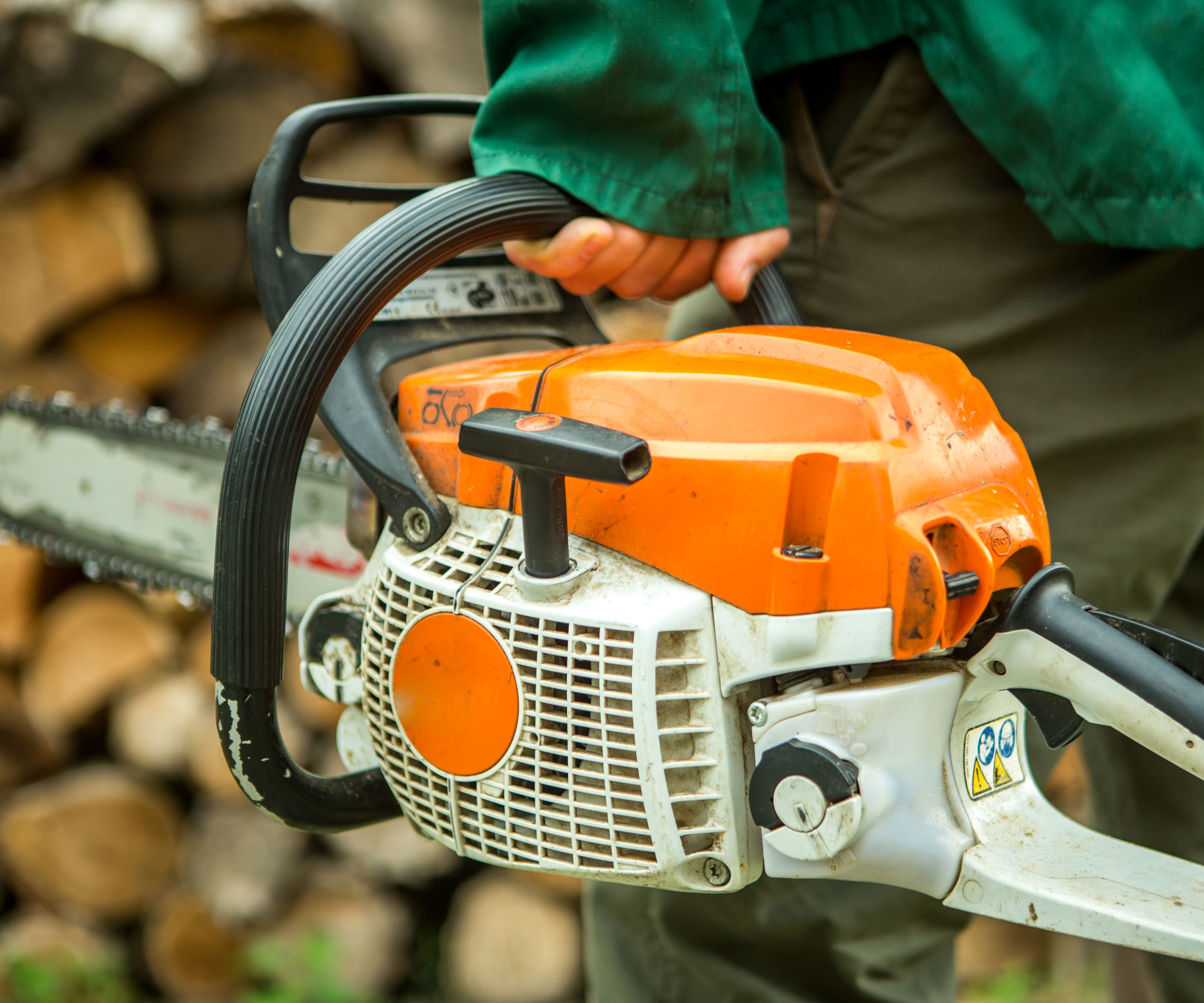 orange chainsaw being held by someone wearing green shirt
