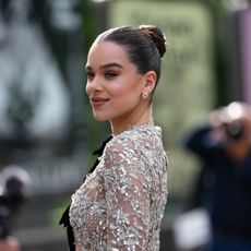 a white woman with dark hair pulled into a bun posing for paparazzi in a sequined mesh gown
