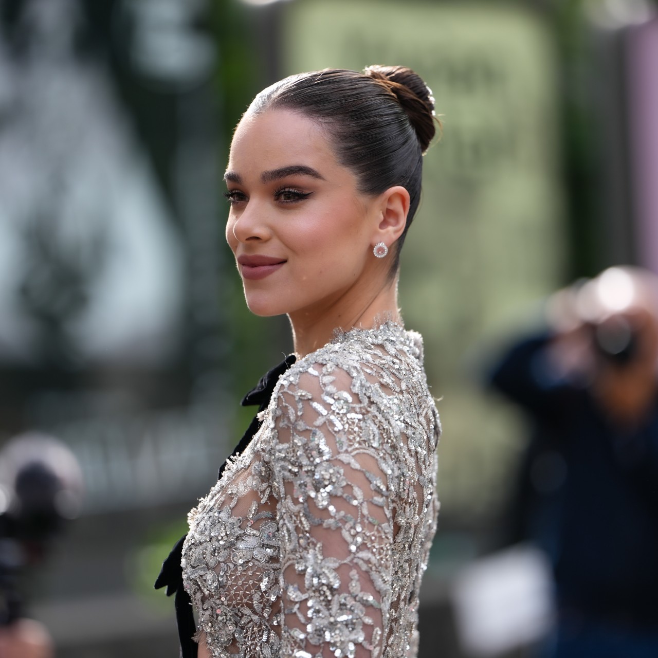 a white woman with dark hair pulled into a bun posing for paparazzi in a sequined mesh gown
