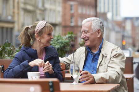 A man and woman smile at each other sitting at an outdoor cafe table in early spring weather.