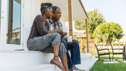 A couple sit on the steps of their home.