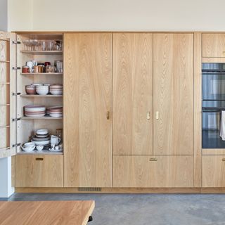 a row of wooden kitchen cabinets with an open door displaying tableware and glassware