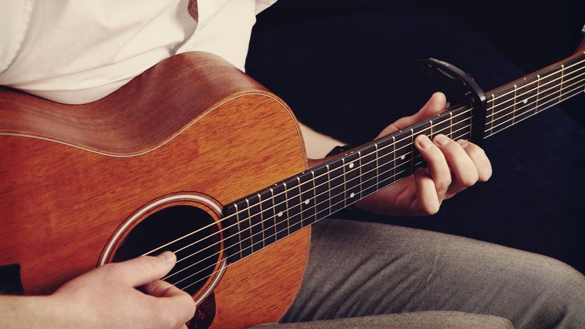 A man plays acoustic guitar with a capo on the neck