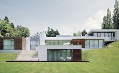 Exterior view of Gerry McGovern's white and wood panelled Warwickshire multi-level home and surrounding greenery during the day