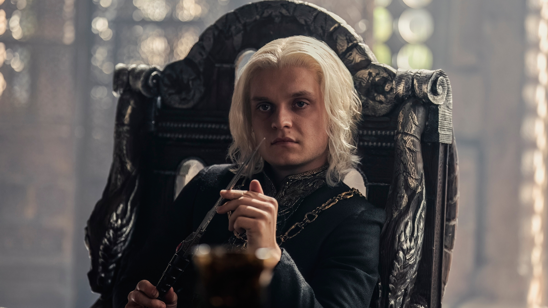 Aegon II (Tom Glynn-Carney) sitting in a chair in the Small Council room in 