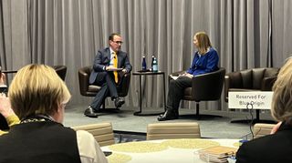 a man and a woman sit on a stage during a "fireside chat" at a conference