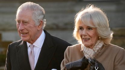 King Charles wears a black coat and white shirt while Queen Camilla wears a camel coat with black leather gloves