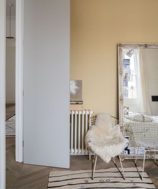 corner of a room with pale yellow wall andc chair in front of mirror