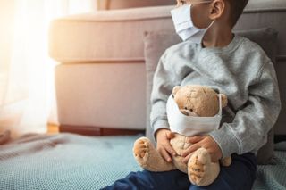 A child with a mask holding a teddy bear with a mask.