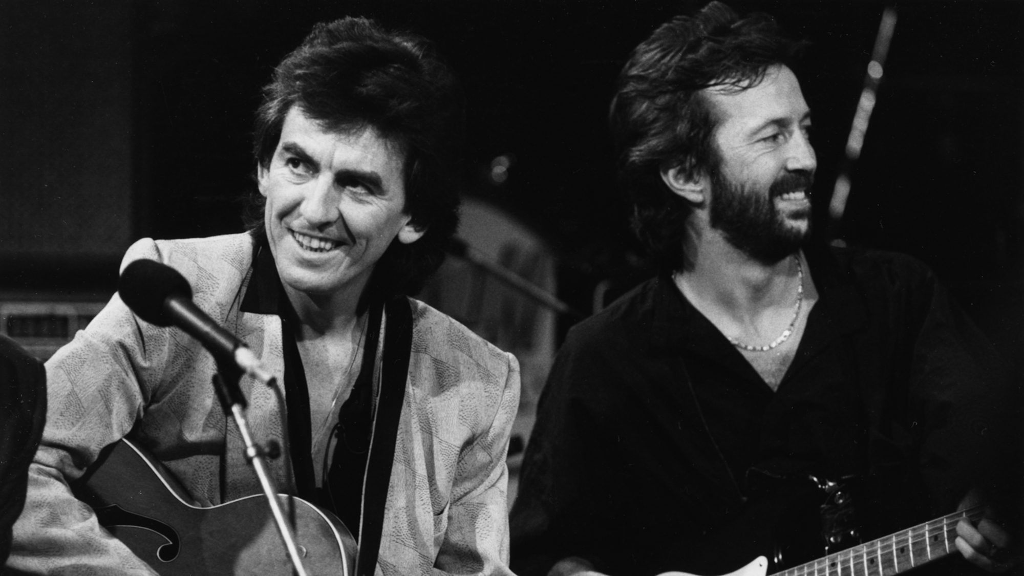 Musicians George Harrison (left) and Eric Clapton performing on stage together as part of an all-star band for music legend Carl Perkins, October 23rd 1985