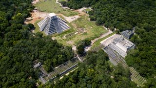 a forest surrounds a large pyramid and other buildings in an aerial view