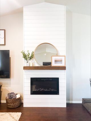 fireplace with white horizontal panelling and a wooden shelf and round mirror