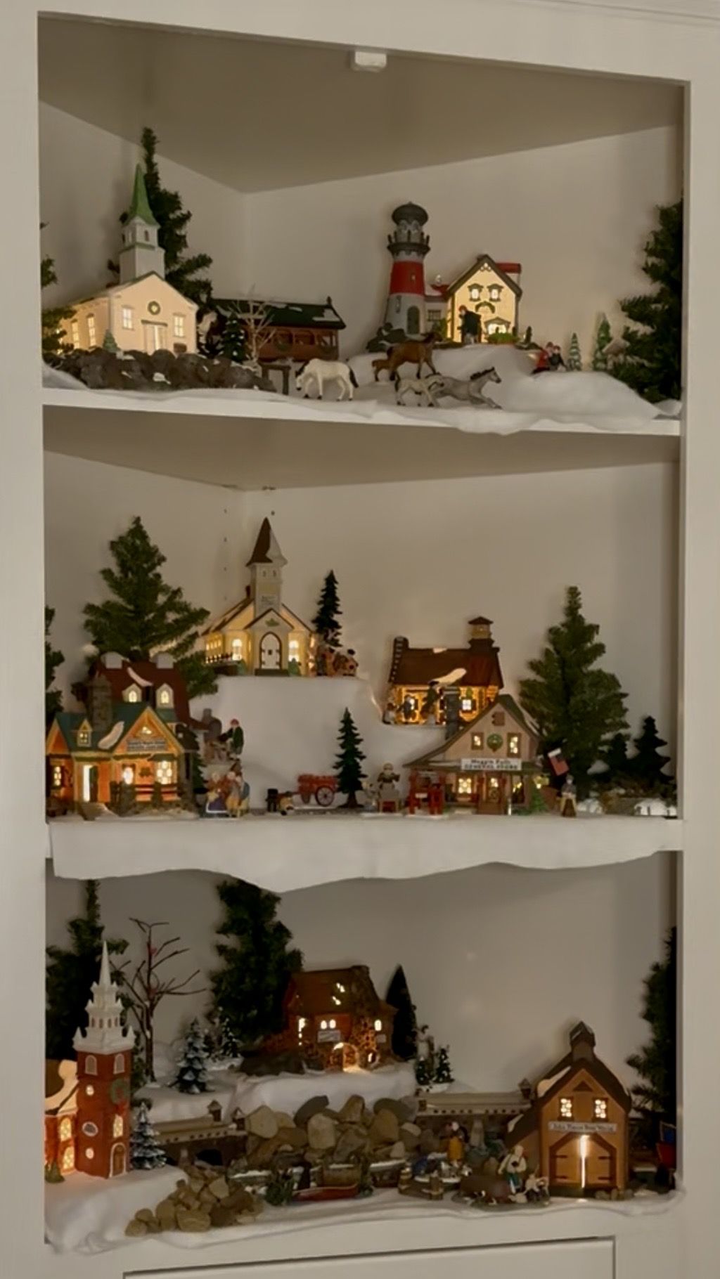 Christmas village displays inside open corner shelving with lit miniature houses, trees fake snow and mini animals and people