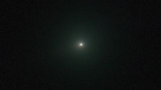 An image of comet 3I/ATLAS appearing as a white dot with a green hue.