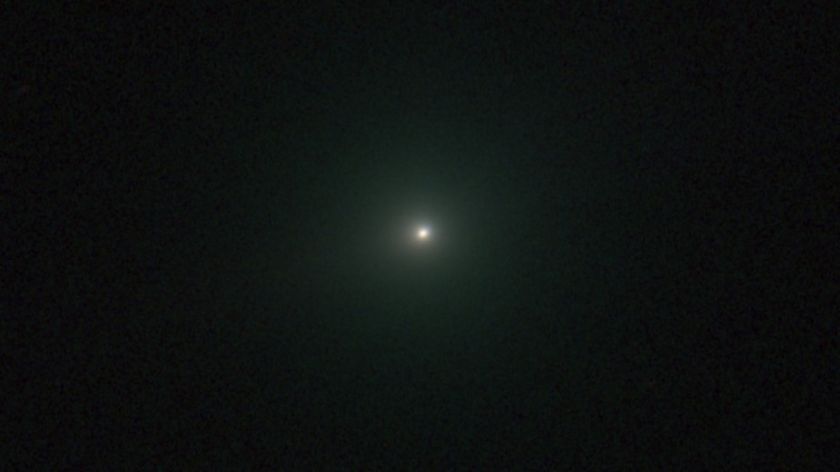 An image of comet 3I/ATLAS appearing as a white dot with a green hue.