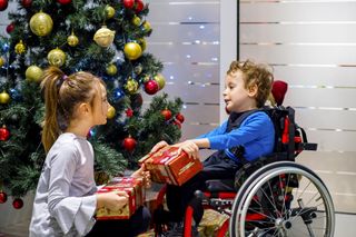 Little boy in wheelchair and his sister opening Christmas gifts