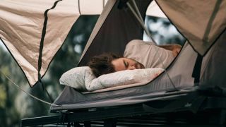 A man sleeping in a tent atop a car