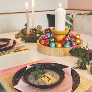 A dinner table set for Christmas with a candle and rainbow bauble centrepiece