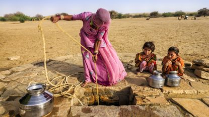 a woman with two children drawing water from a well in the desert
