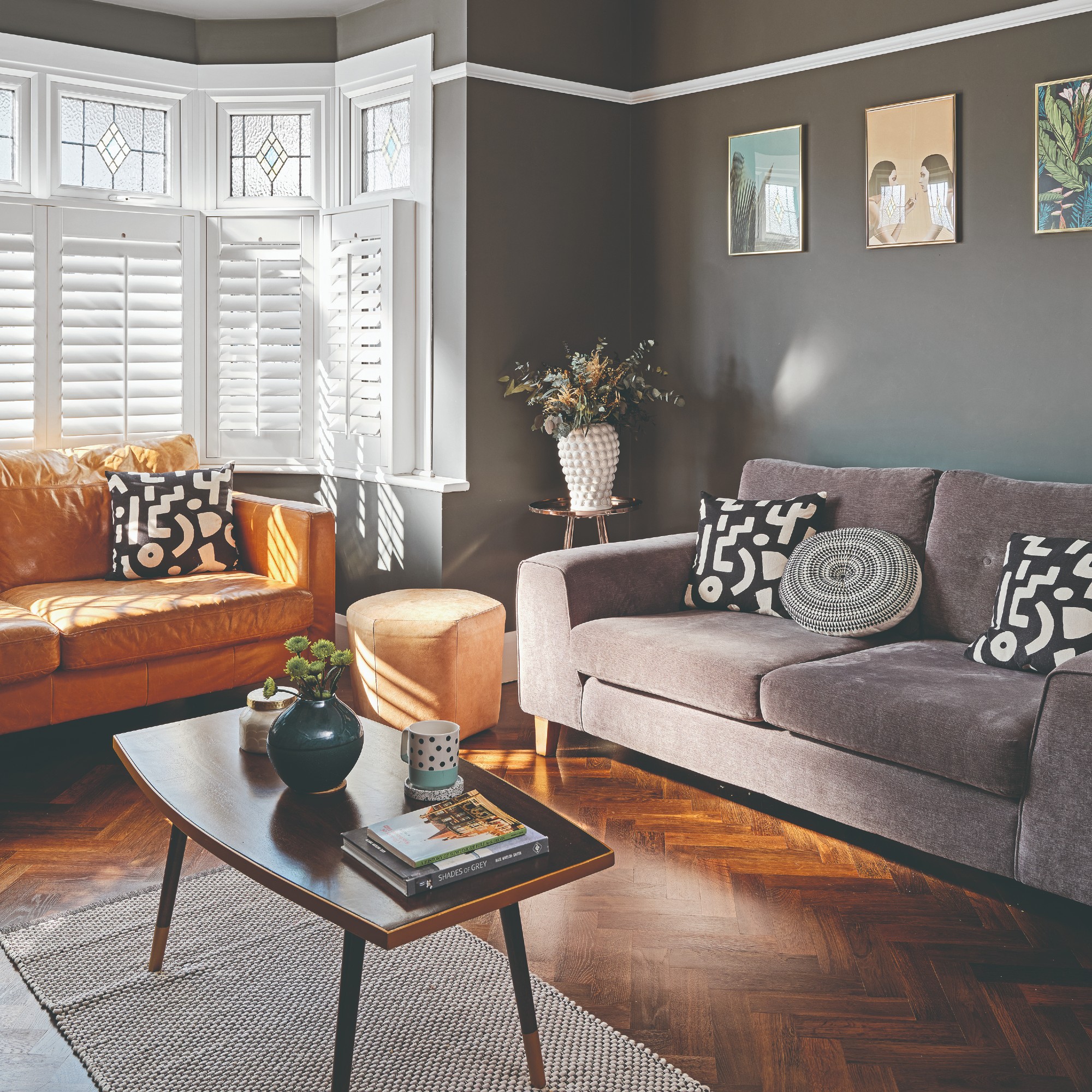 A dark grey-painted living room with a grey velvet sofa, a tan leather sofa and a small stool