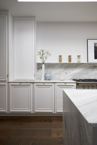 A kitchen with white marble countertops and white cabinetry