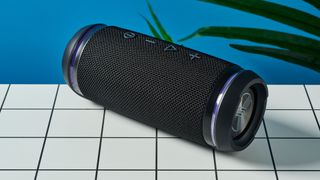 a black portable bluetooth speaker with LED panels sits atop a white table with a blue background