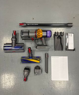 All parts and attachment heads of the Dyson V15 Detect Absolute positioned on a gray linoleum floor in Future's testing center