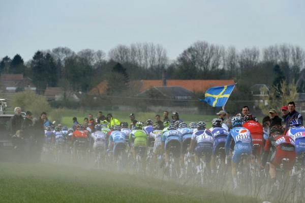 The peloton in a dusty section of cobbles