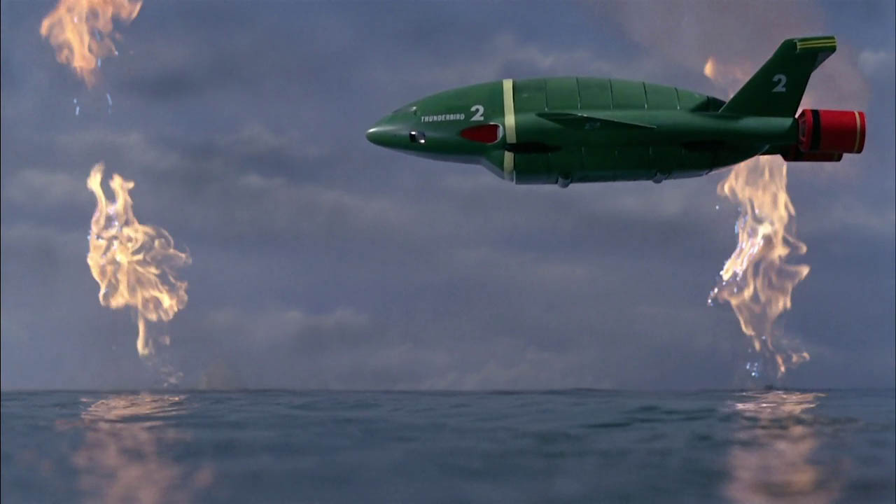 Screenshot from Thunderbirds showing Thunderbird 2 flying over water.
