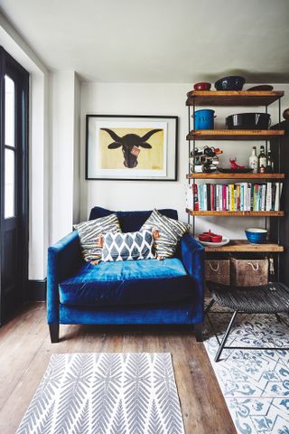 A living room with blue velvet armchair sofa decor, wooden flooring, framed wall art and blue/white living room floor tiles