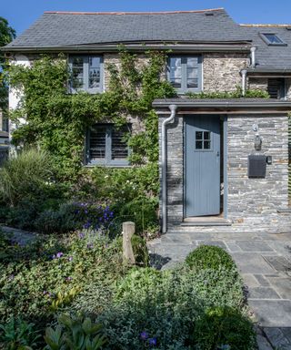 A traditional stone house with a dark gray front door and a green front garden