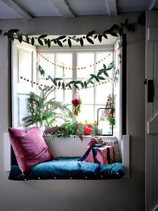 a window in a kitchen dressed for Christmas with garlands and velvet cushions and seat