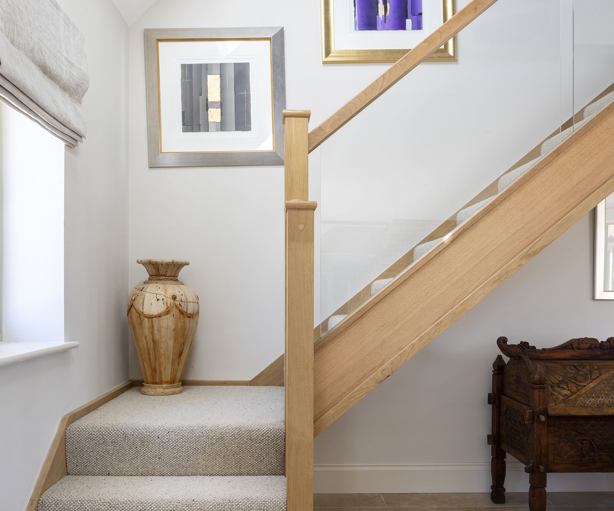 A wood and glass staircase with cream carpet and light walls with framed artwork on the walls