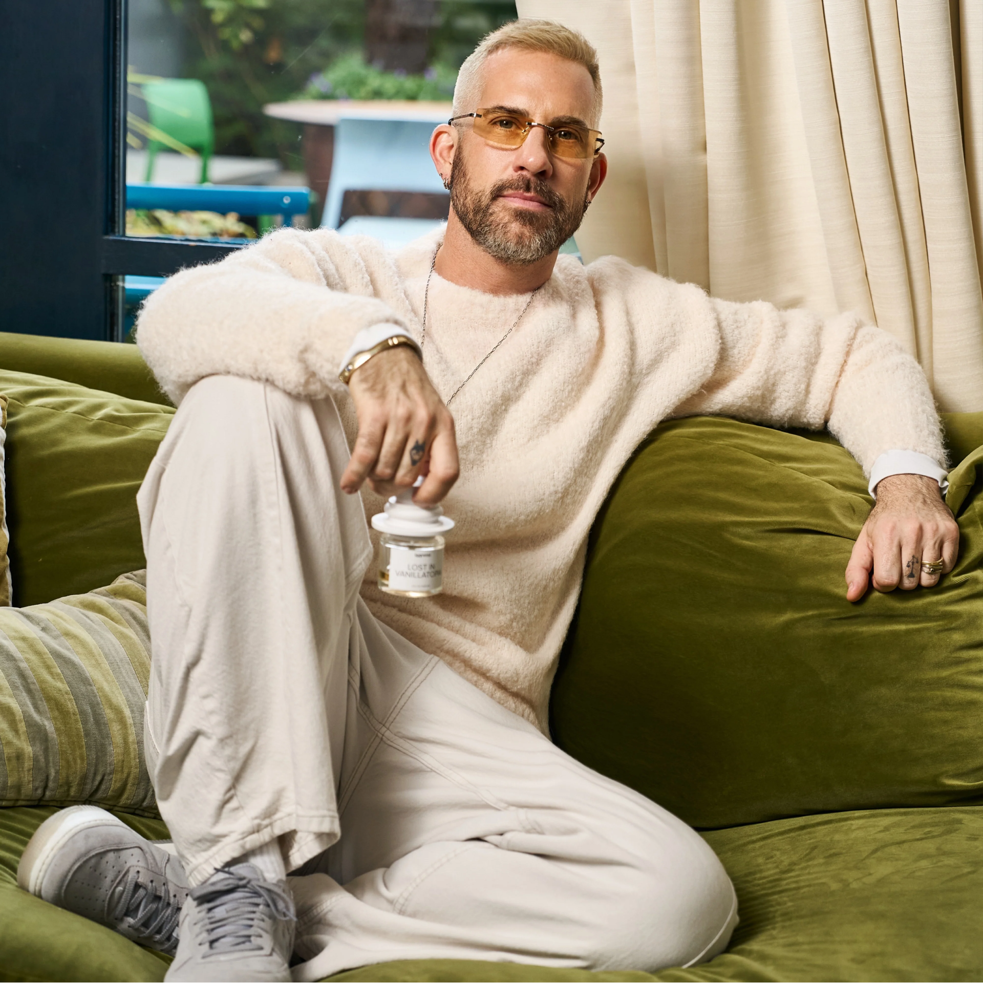 Richard Saint-Ford poses on a velvet green couch with a bottle of Iggywoo fragrance.