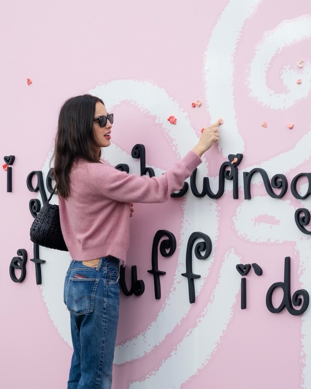 Olivia Rodrigo wears a pink Doen cardigan with blue jeans and a white T-shirt and carries a black woven bag