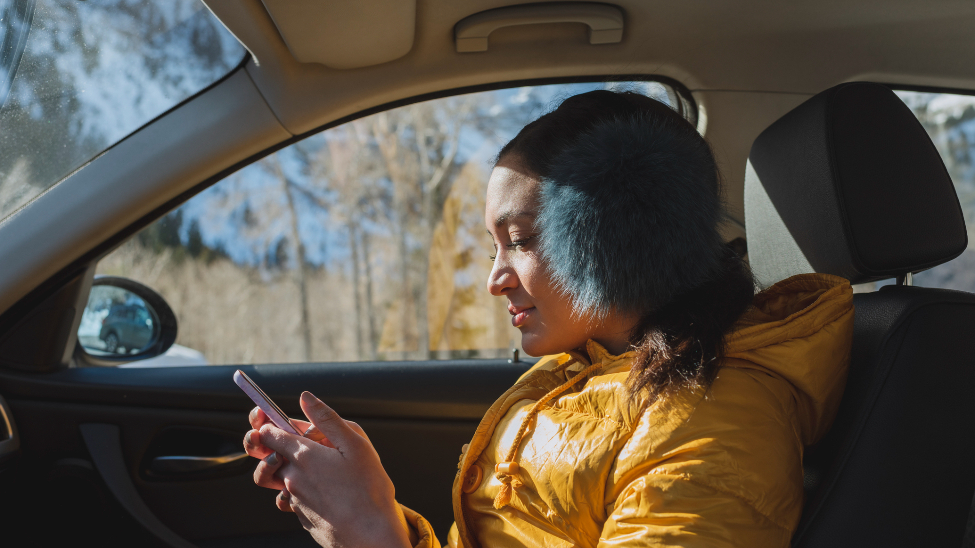 A person, looking at their phone in the car in a wooded area.