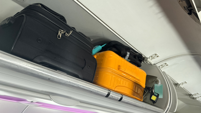 A yellow suitcase and a black suitcase in an overhead compartment on a plane