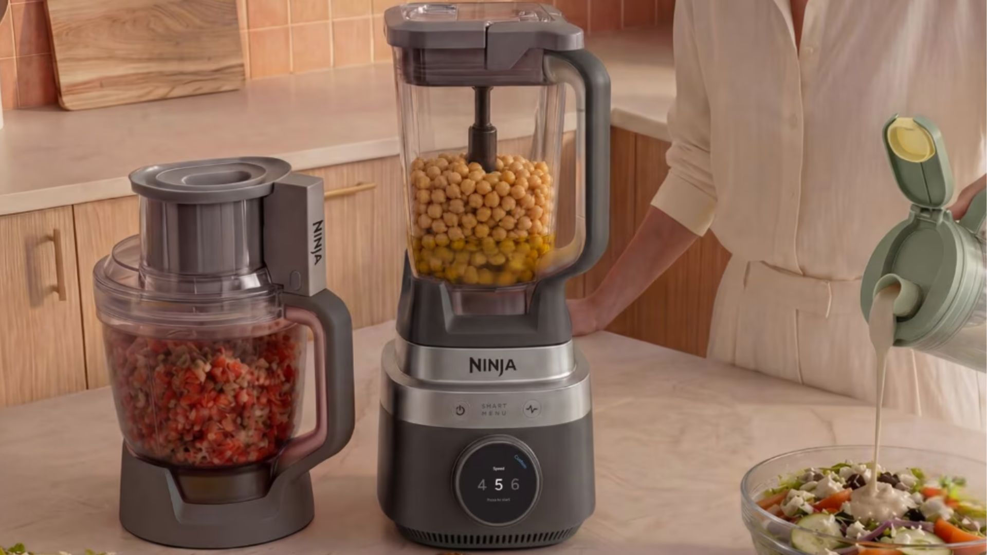 Ninja CrushBOSS 3-in-1 Kitchen System on the counter making a smoothie, chopping vegetables, and pouring dressing over a salad