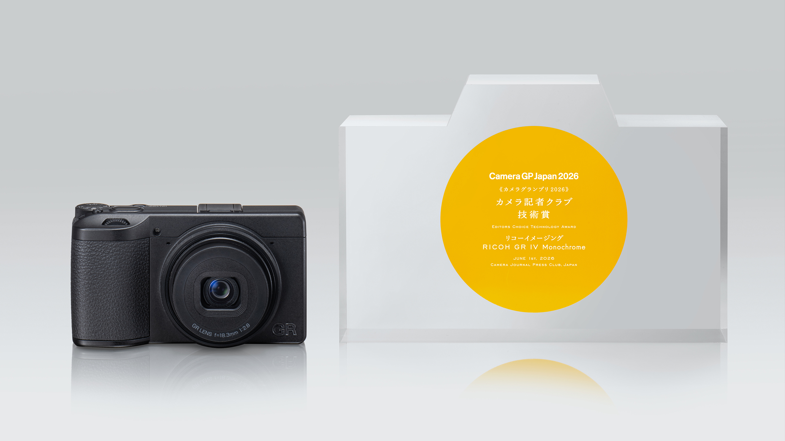 Black Ricoh GR IV Monochrome camera beside a Camera GP Japan 2026 award shaped like a camera with a yellow circular label