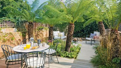 Wooden bench in front of garden wall with potted plants around a stump table 