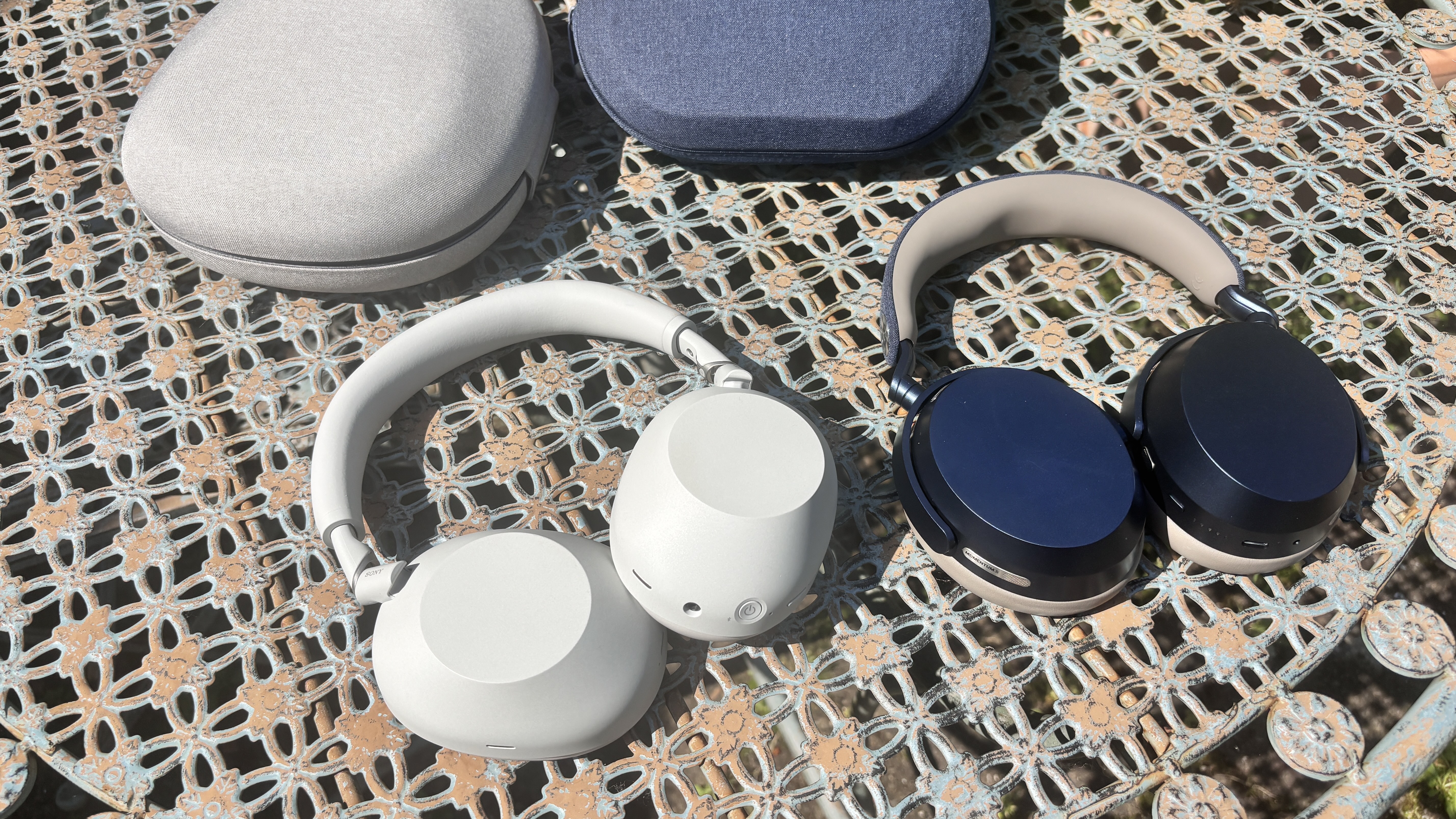 Sony WH-1000XM6 and Sennheiser Momentum 5 Wireless headphones placed side by side on a table outside