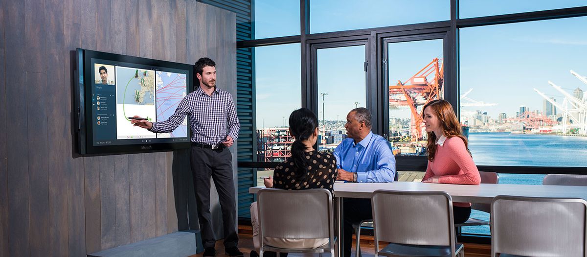 Man pointing to a screen on the wall of a boardroom with his colleagues sitting at the table