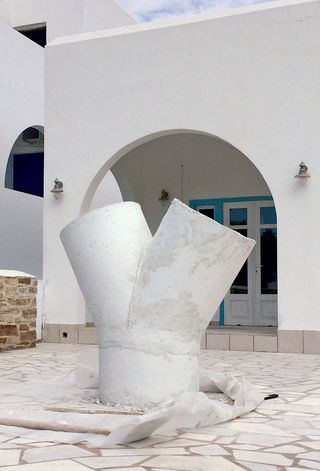 Three-way, white concrete pipe standing in a courtyard in front of an arched doorway