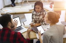 A high-point shot of three students in an IT course talking around desks and laptops