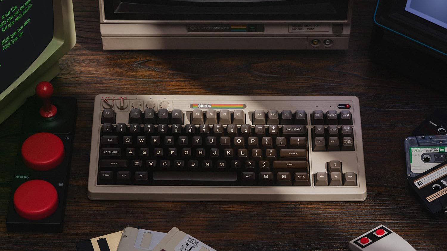 8BitDo Retro Mechanical Keyboard C64 Edition on top of wooden desk with controllers, floppy disks and monitors surrounding it