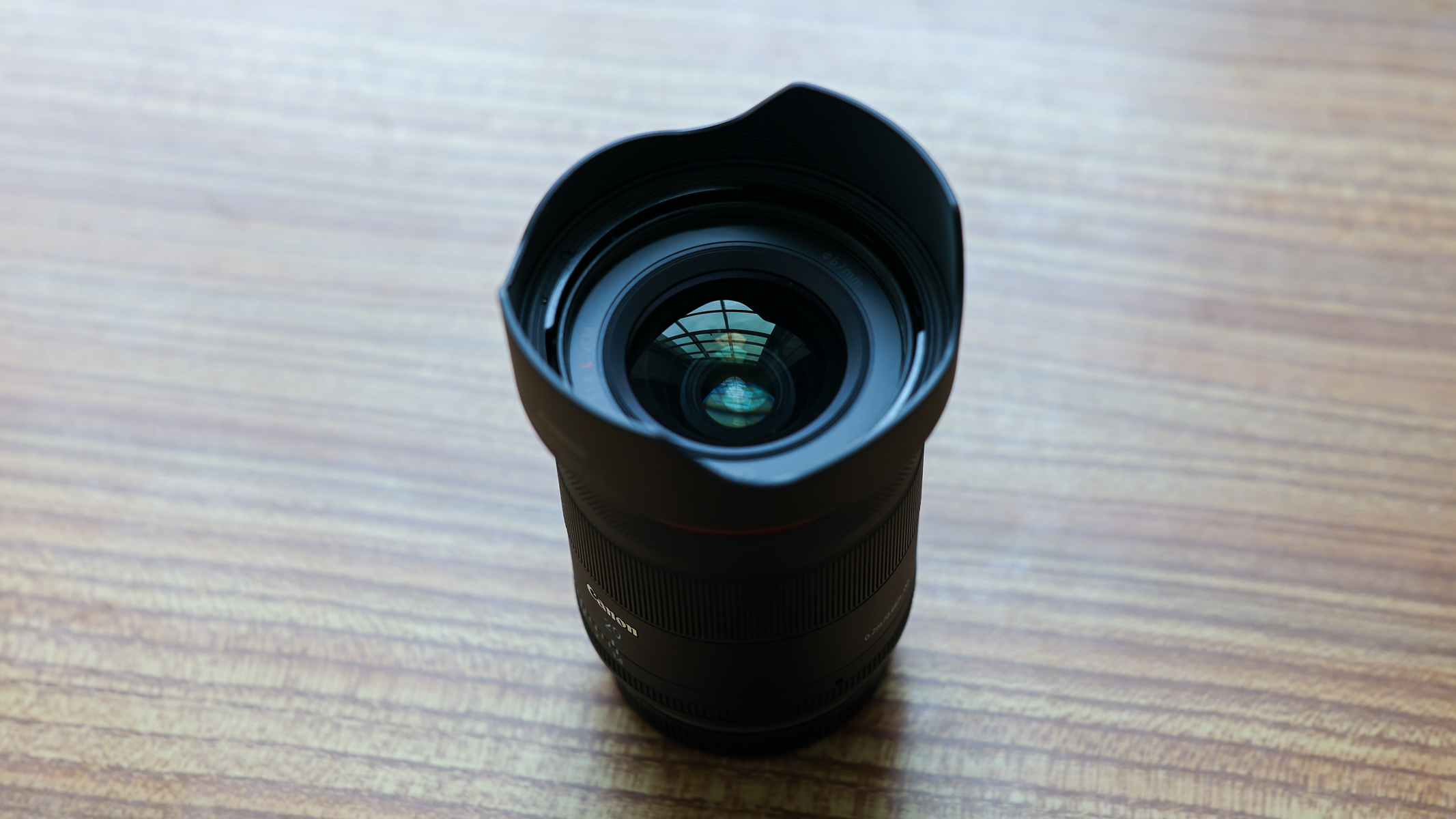 The Canon RF 20mm f/1.4 L VCM lens with lens hood on a wooden table.