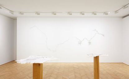 White room, wooden floor, white spotlights on a frame around the edge of the ceiling, two wooden posts topped with white model exhibition piece