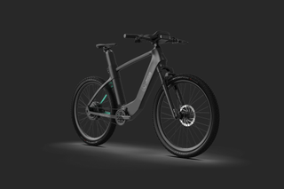 A matte black e-bike with flat handlebars sits at a 30* angle to the camera with a black background.
