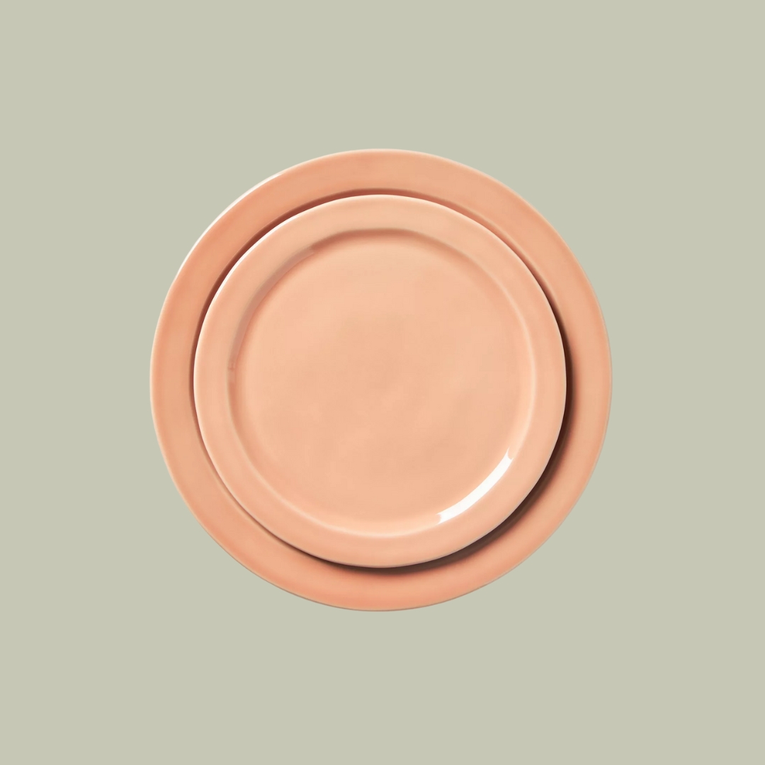 Two terracotta-hued, glazed ceramic plates stacked on top of each other against pale green background.